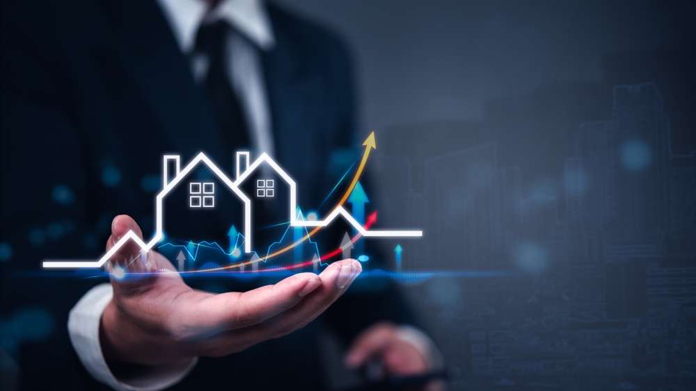 Symbolbild: Hand hält aufsteigende Diagramme mit Häusern – Nachhaltigkeit im Fokus der Immobilienpreise München 2025