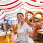 Lebensqualität in München – Frau im Dirndl mit Brezel und Bier auf dem Oktoberfest