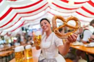 Lebensqualität in München – Frau im Dirndl mit Brezel und Bier auf dem Oktoberfest