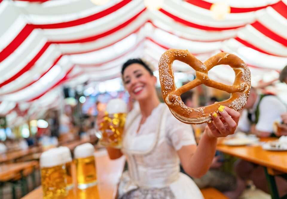 Lebensqualität in München – Frau im Dirndl mit Brezel und Bier auf dem Oktoberfest