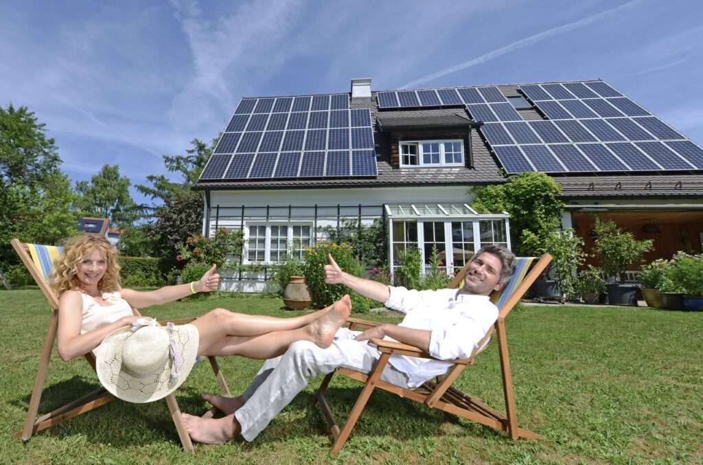 Paar entspannt im Garten vor einem Haus mit Solarpanelen – Symbol für Energieeffizienz und Immobilienpreise in München 2025