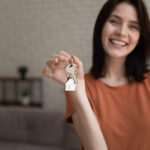 Frau mit Schlüsselanhänger in Hausform – Symbol für Immobilienerbe oder Immobilien als Kapitalanlage