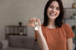 Frau mit Schlüsselanhänger in Hausform – Symbol für Immobilienerbe oder Immobilien als Kapitalanlage