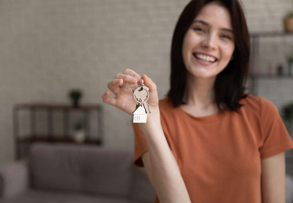 Frau mit Schlüsselanhänger in Hausform – Symbol für Immobilienerbe oder Immobilien als Kapitalanlage