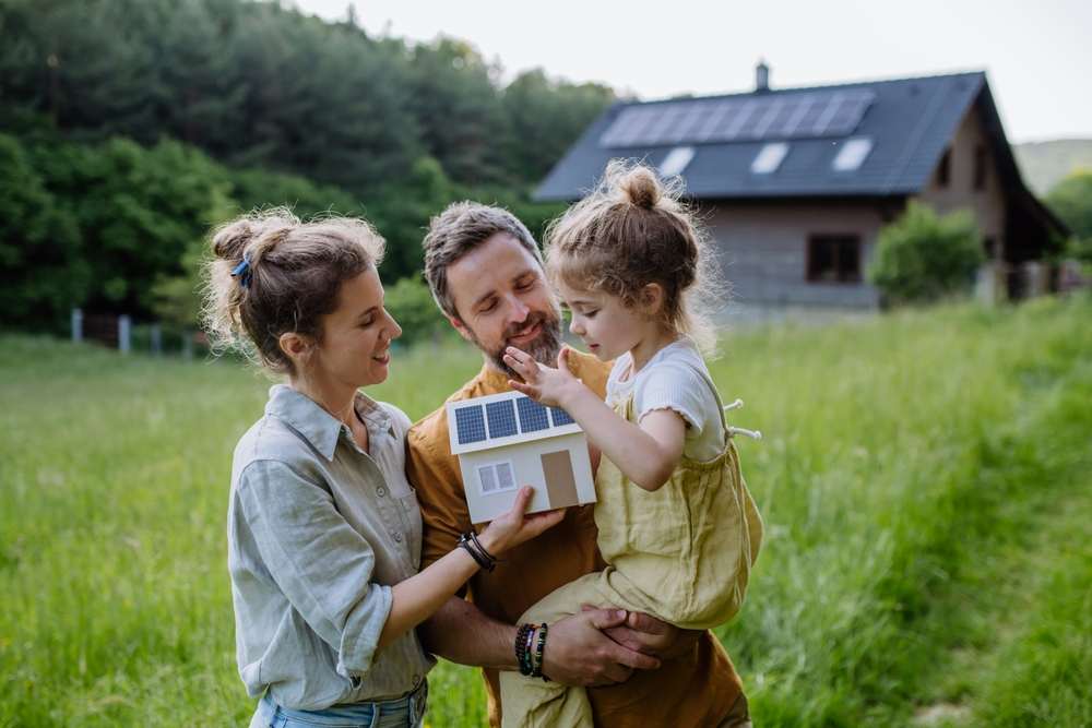 Familie mit Modellhaus im Grünen – Symbol für nachhaltiges Bauen in München